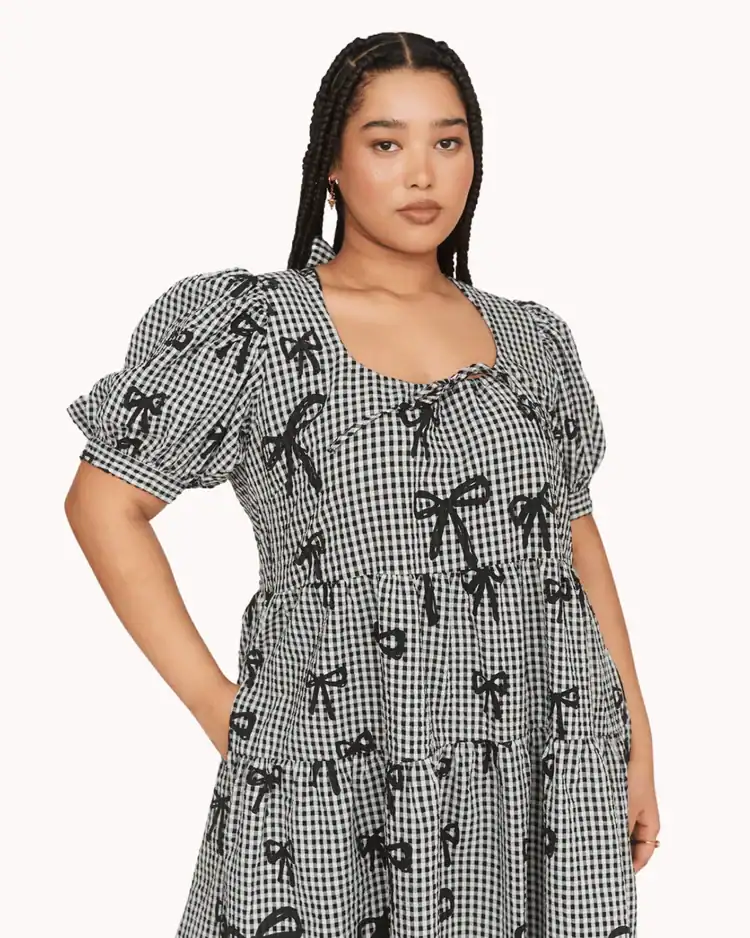 Model poses wearing checkered black dress with black bows