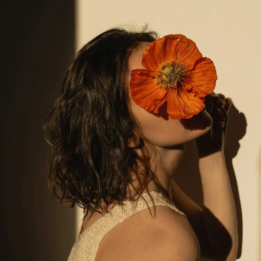 Woman-holding-a-large-orange-flower-to-her-face-in-a-dimly-lit-room