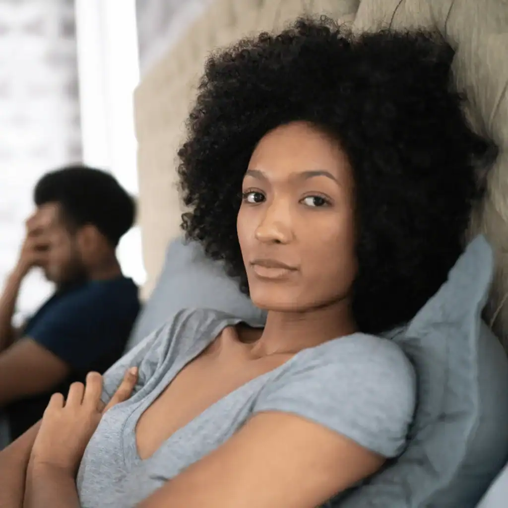 Woman-with-afro-looks-fed-up-she-is-sitting-up-beside-her-partner-in-bed