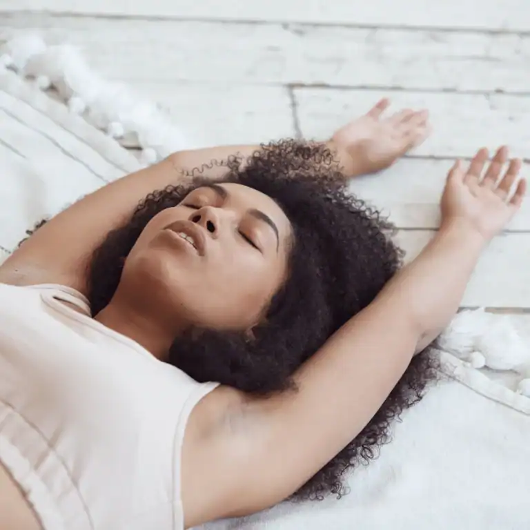 Woman-with-curly-hair-laying-down-with-her-hands-stretched.Somatic-Breathing