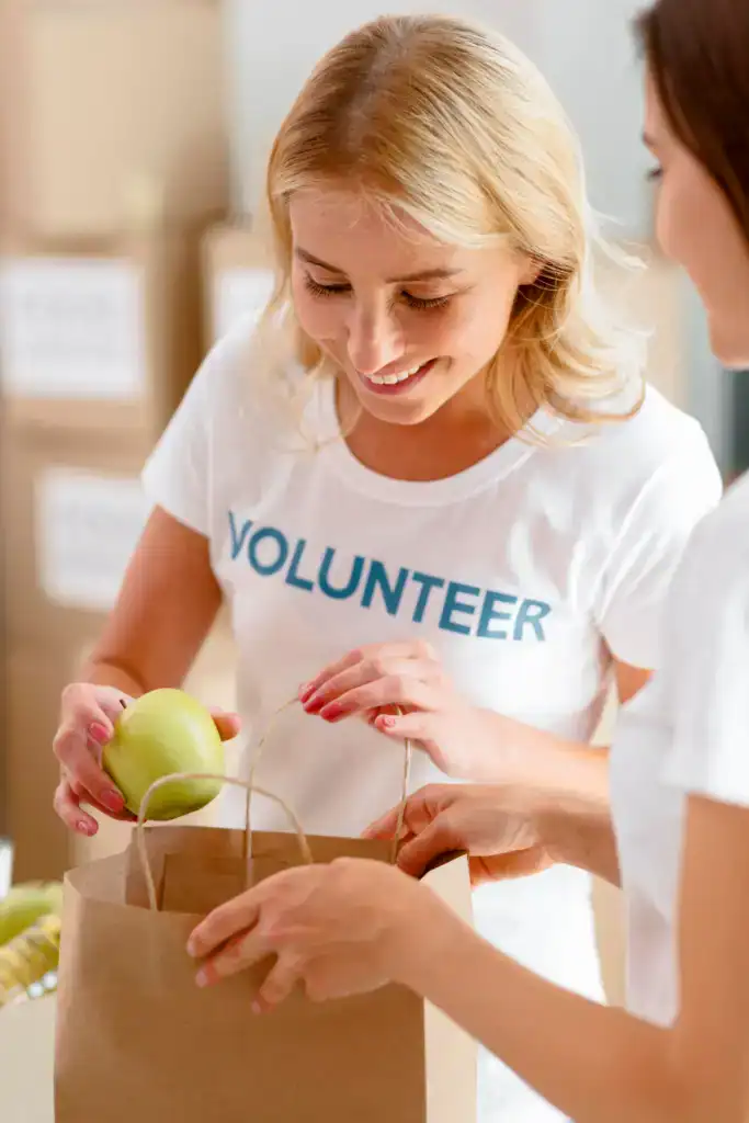 smiley-female-volunteers-putting-food-bag-donation