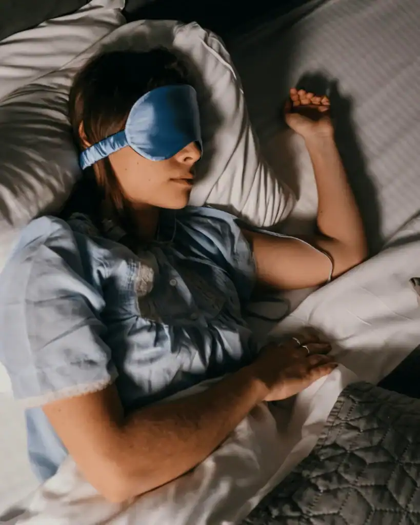 young-white-woman-sleeping-in-a-bed-wearing-blue-satin-eye-mask.-Lighting-is-dim.-Pillow-Method